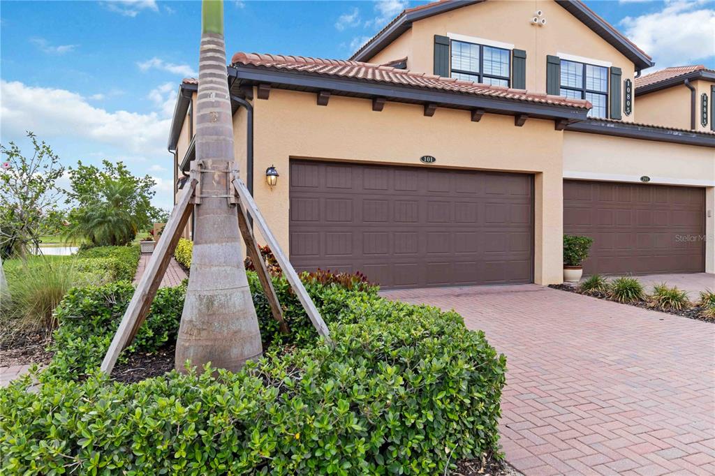 A two-story stucco townhouse features a brown garage door and a brick paver driveway — 10805 TARFLOWER DRIVE UNIT 101, VENICE, FL