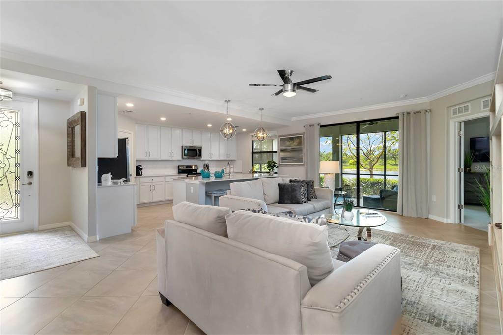 An open-concept living room and kitchen featuring white cabinetry, light tile flooring, and sliding doors — 10805 TARFLOWER DRIVE UNIT 101, VENICE, FL