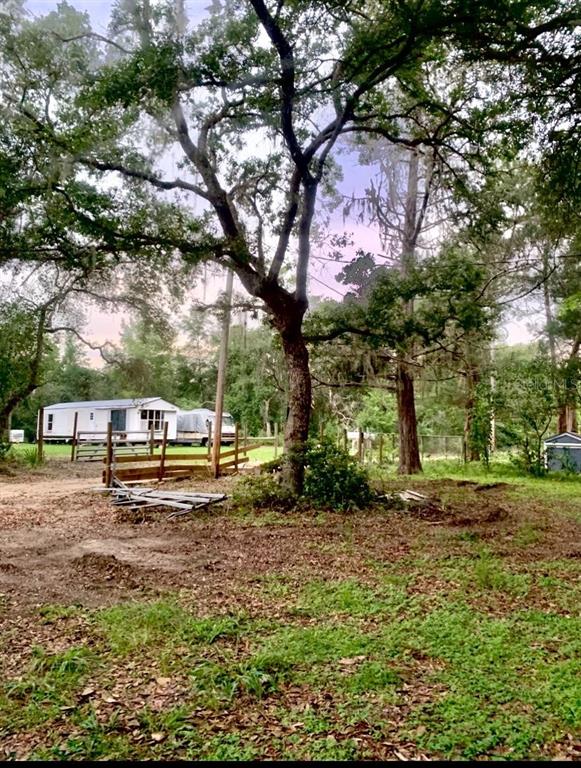 A mobile home sits on a grassy lot behind a wooden fence and large trees — 17273 NE 37TH STREET, SILVER SPRINGS, FL