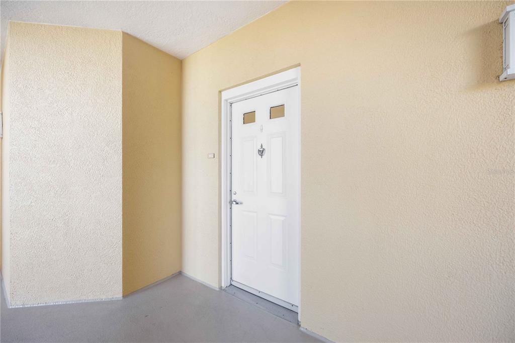 A white front door with two small windows is set into a beige stucco wall — 606 RIVIERA DUNES WAY UNIT 302, PALMETTO, FL