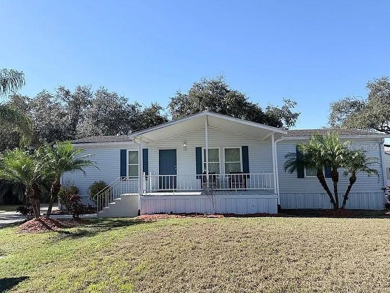A single-story manufactured home with light siding, a front porch, and palm trees in the yard — 2086 STARBOARD DRIVE, GENEVA, FL