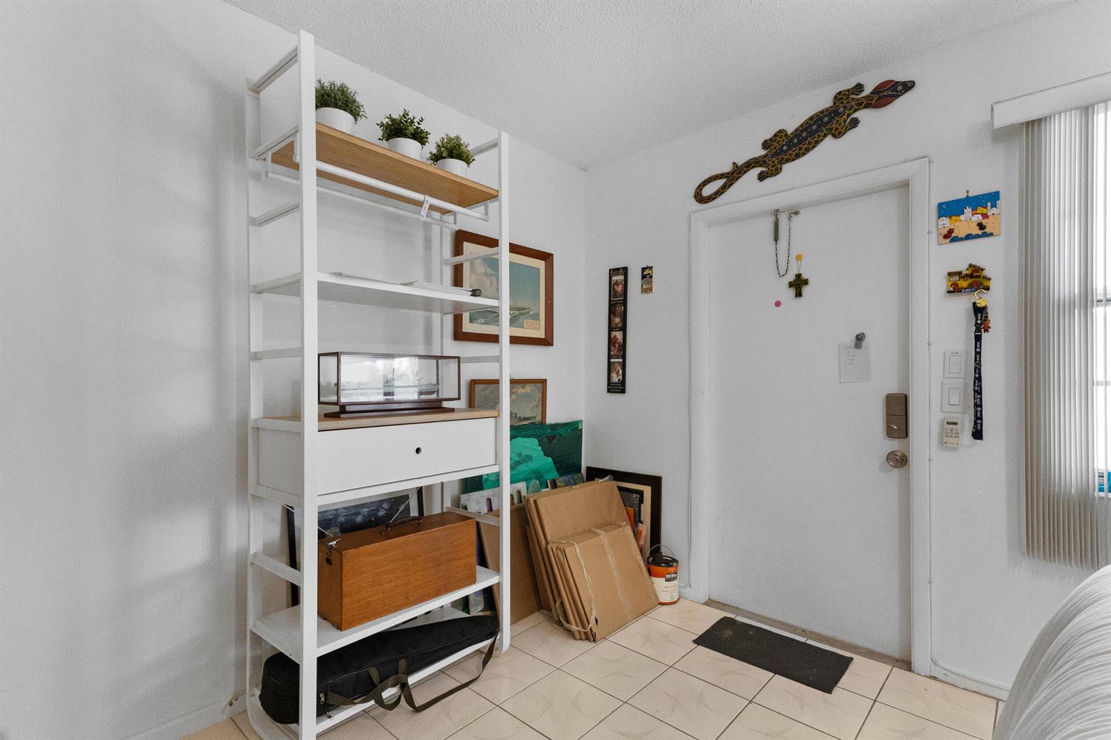 An entryway features a white metal shelving unit, tiled floors, and a white door — 18 Prescott A, Deerfield Beach FL 33442, DEERFIELD BEACH, FL