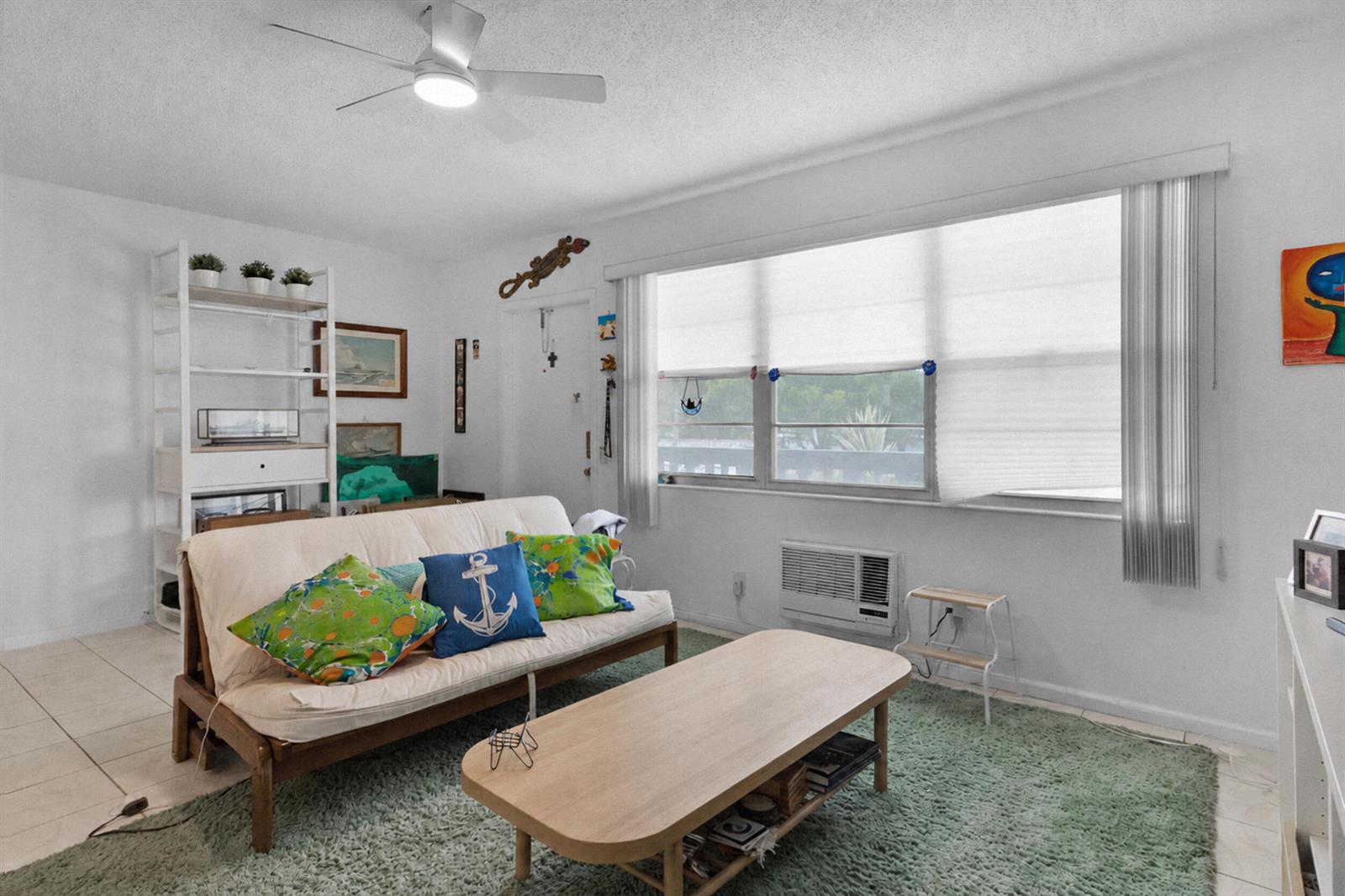 A living room features a futon, a coffee table, a green rug, and a window — 18 Prescott A, Deerfield Beach FL 33442, DEERFIELD BEACH, FL