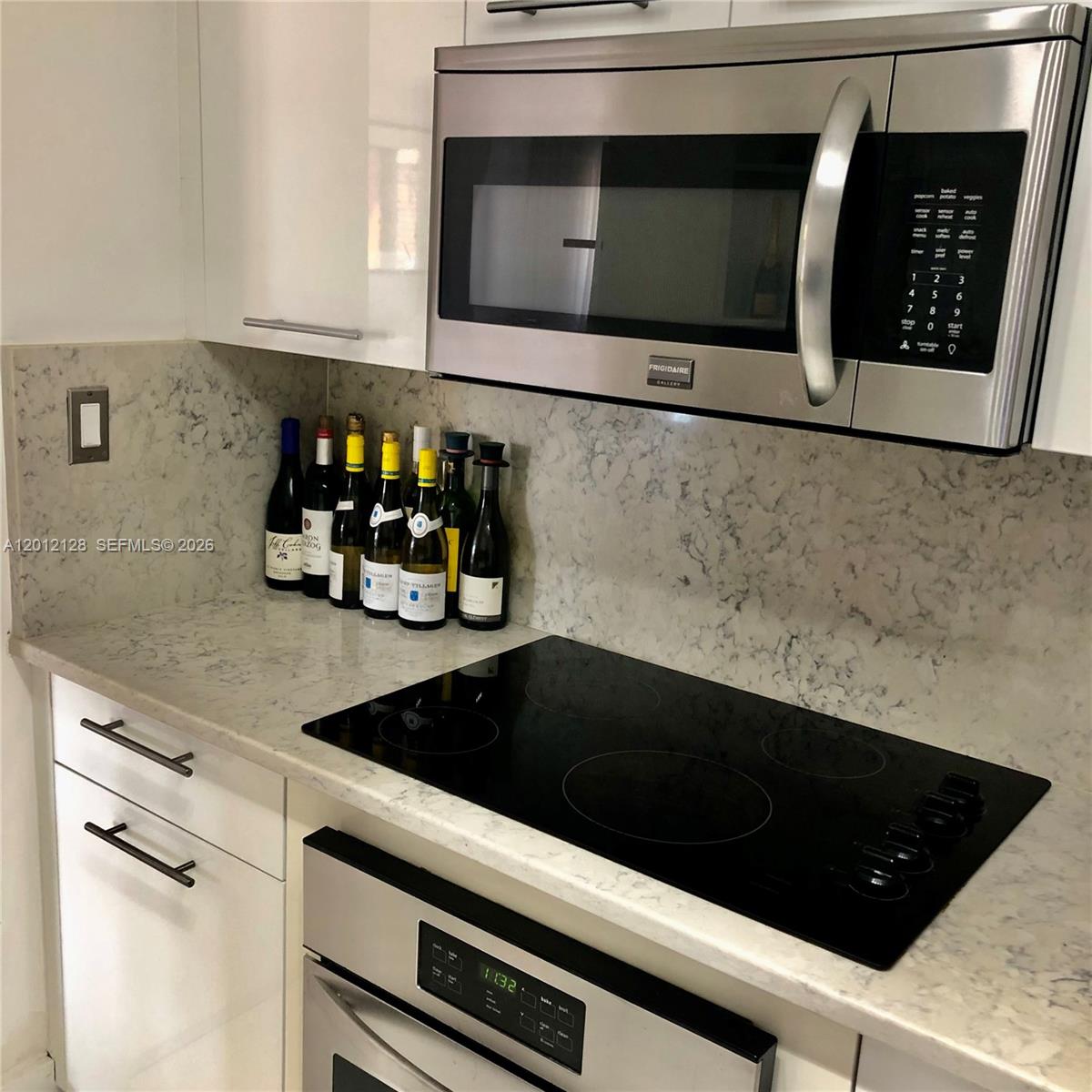 A kitchen features white cabinets, a stainless steel microwave, a glass cooktop, and marble countertops — 90 Alton Rd # 307, Miami Beach FL 33139, MIAMI BEACH, FL