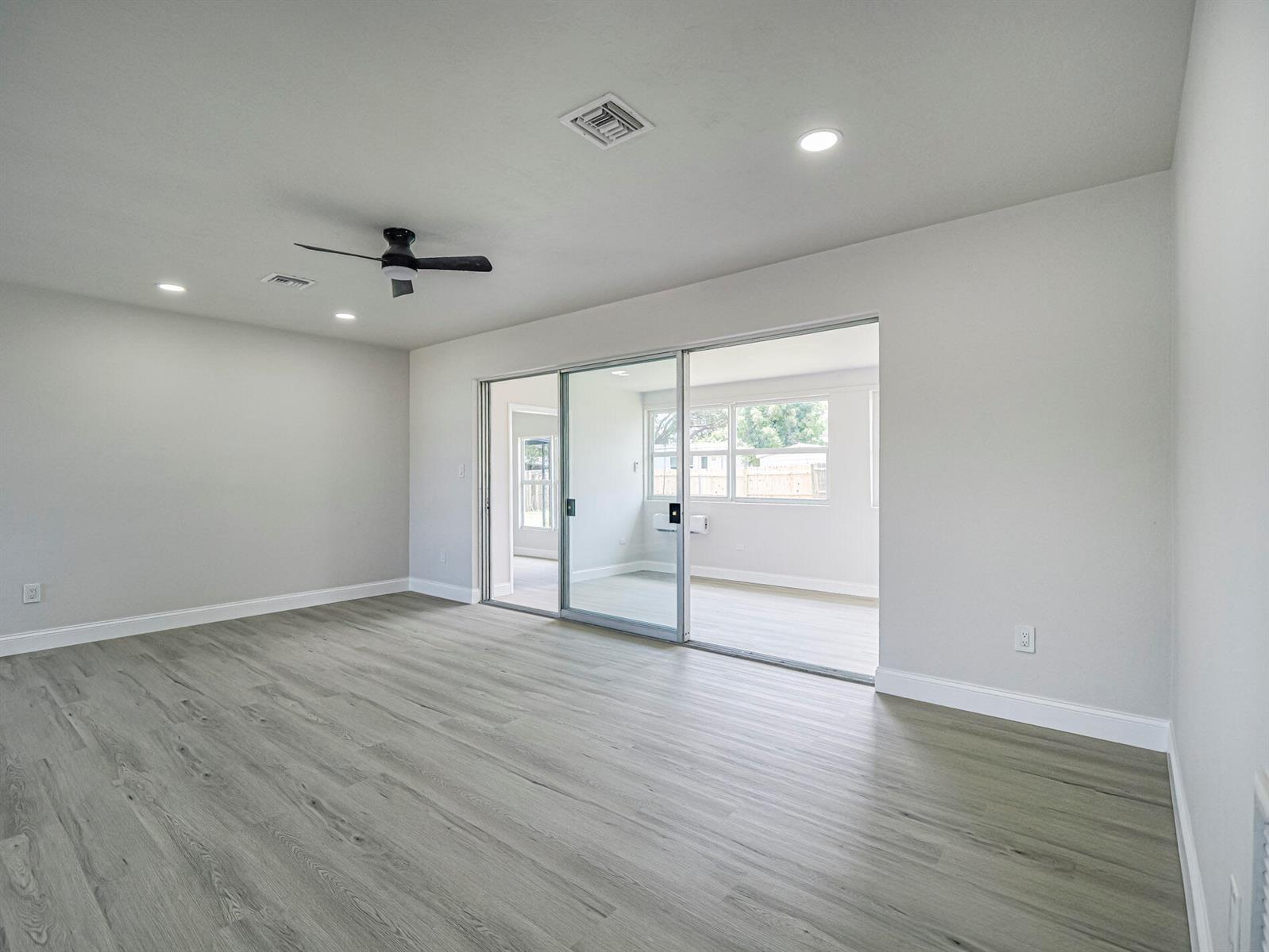 A bright, empty room with gray wood-look flooring, a ceiling fan, and sliding glass doors — 375 Manly Avenue, Sebastian FL 32958, SEBASTIAN, FL