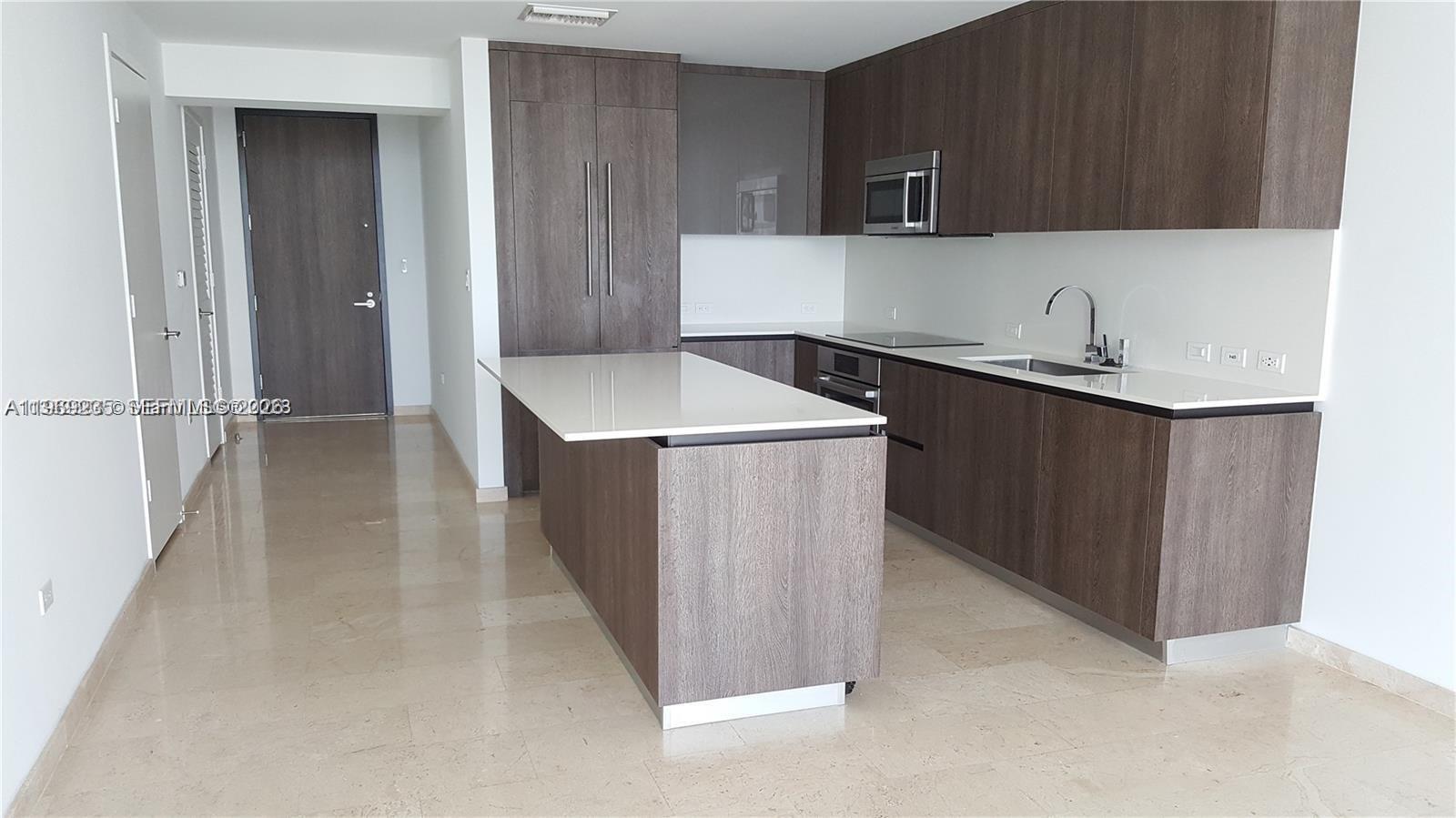 A modern kitchen features dark wood cabinetry, a white countertop island, and light tile flooring — 68 SE 6th St # 3305, Miami FL 33131, MIAMI, FL