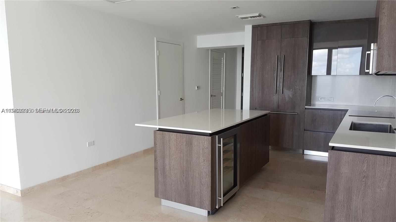 A modern kitchen features dark wood cabinetry, a white quartz island, and light stone flooring — 68 SE 6th St # 3305, Miami FL 33131, MIAMI, FL