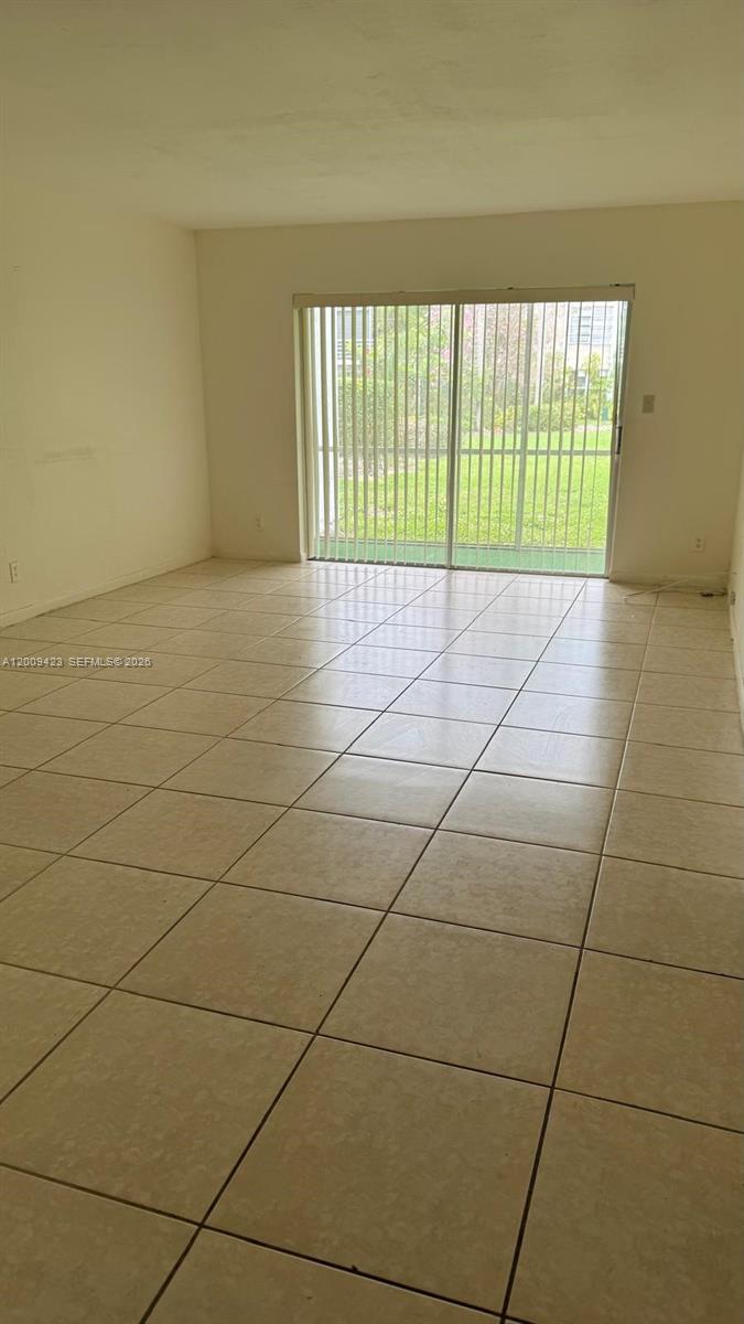An empty room features light-colored floor tiles and a sliding glass door leading outside — 3774 Inverrary Blvd # 105P, Lauderhill FL 33319, LAUDERHILL, FL