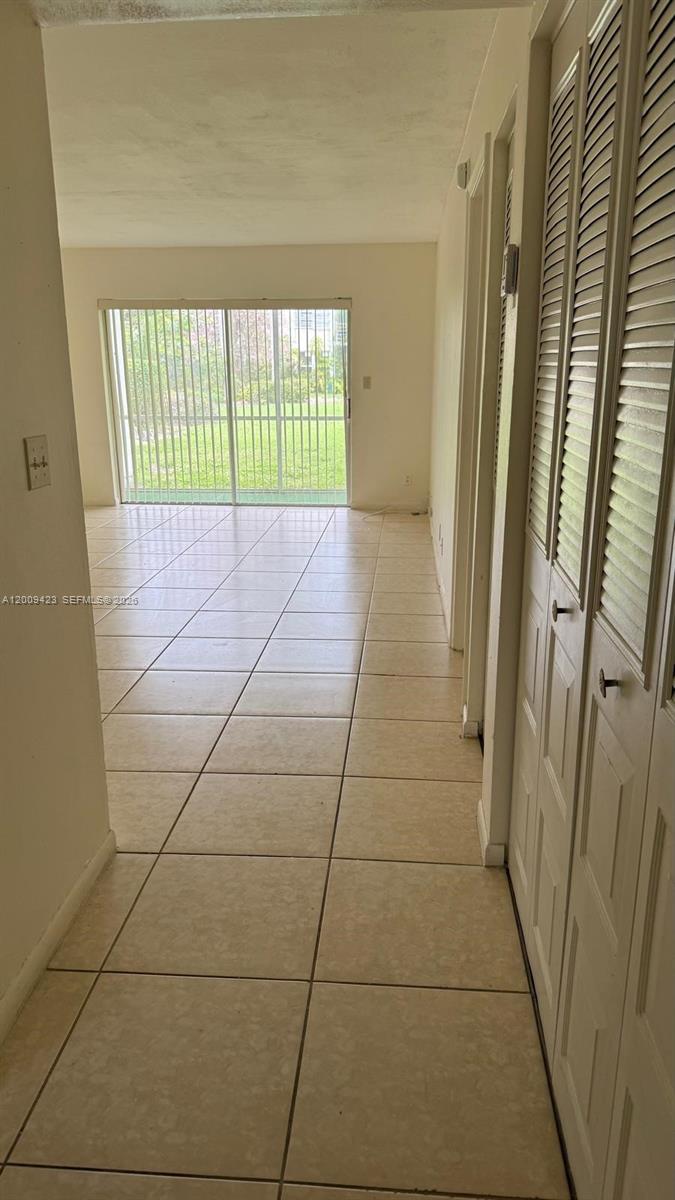 A hallway with tiled floors leads to a living area with sliding glass patio doors — 3774 Inverrary Blvd # 105P, Lauderhill FL 33319, LAUDERHILL, FL