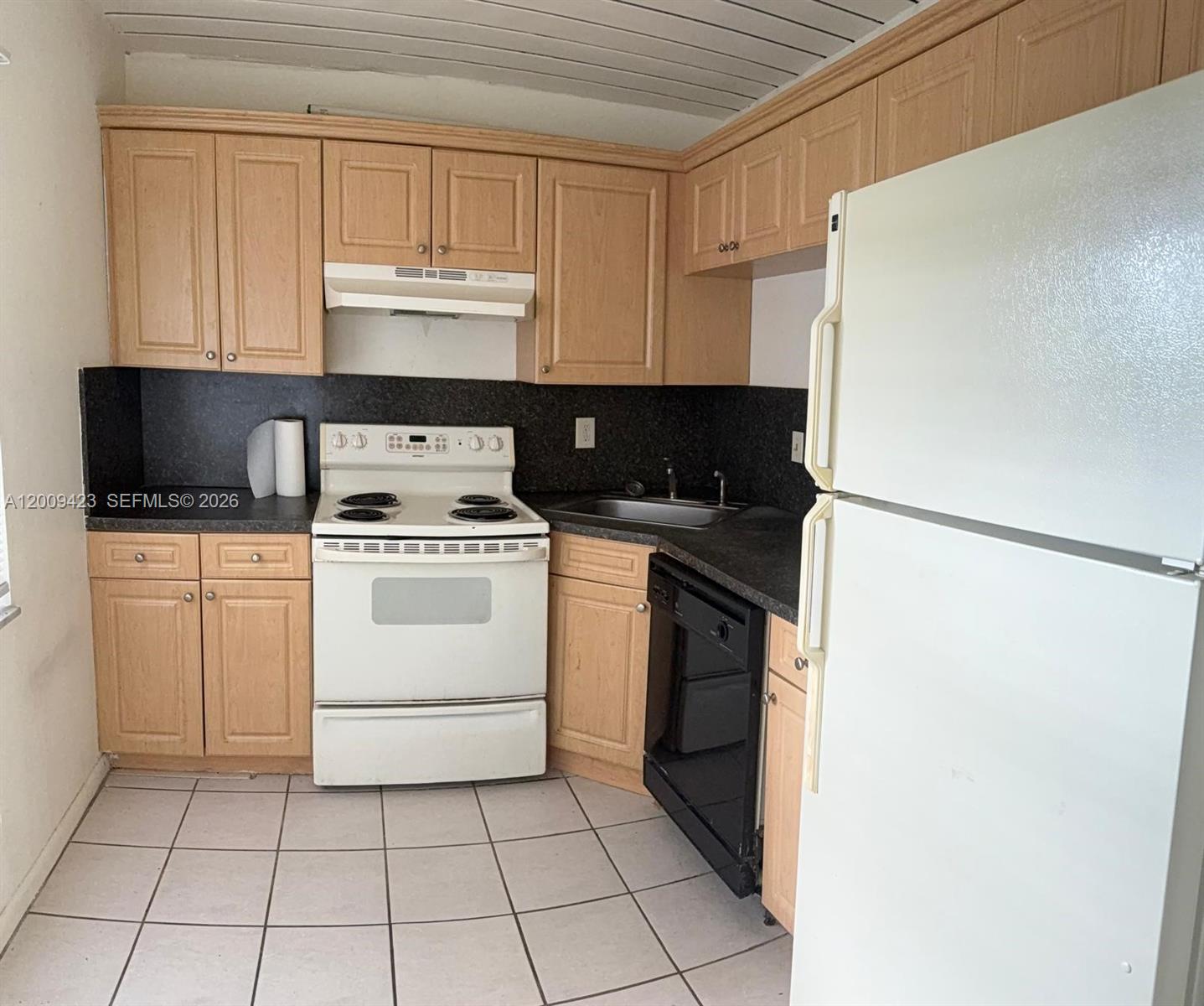 A kitchen features light wood cabinets, dark countertops, white appliances, and white floor tiles — 3774 Inverrary Blvd # 105P, Lauderhill FL 33319, LAUDERHILL, FL