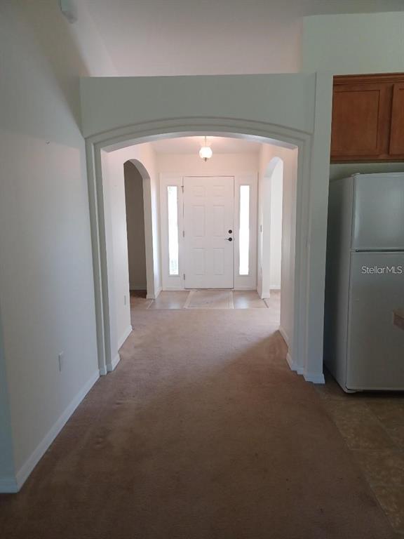 A carpeted hallway leads to a white front door framed by an arched entryway — 63 BANNBURY LANE, PALM COAST, FL
