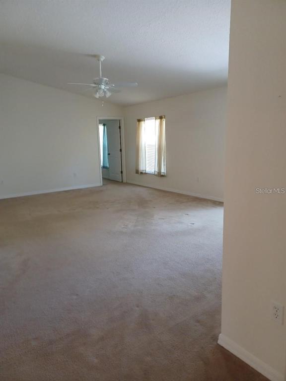 An empty room with beige carpeting, white walls, a ceiling fan, and a doorway — 63 BANNBURY LANE, PALM COAST, FL
