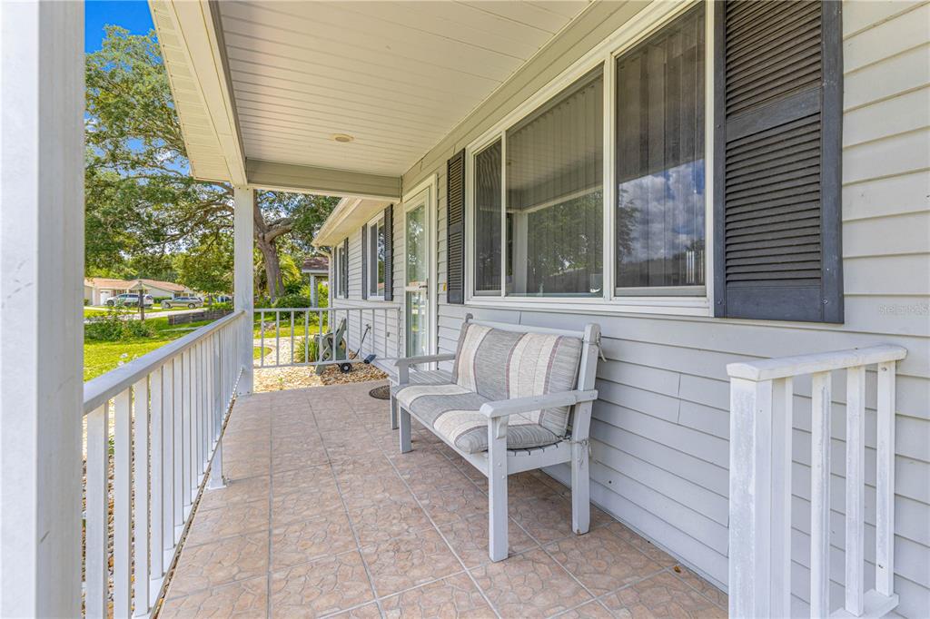 A covered front porch with tiled flooring, a wooden bench, and white railings — 8208 SW 108TH LANE ROAD, OCALA, FL