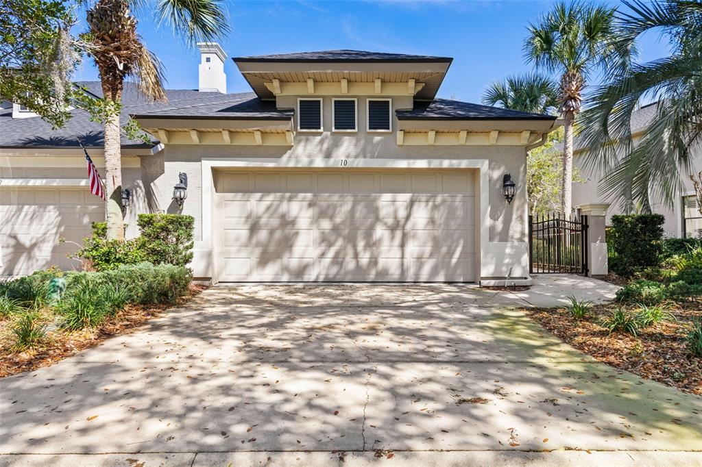 A beige two-car garage with a decorative roofline and a concrete driveway under palm trees — 10 RIVER POINT DRIVE, PALM COAST, FL