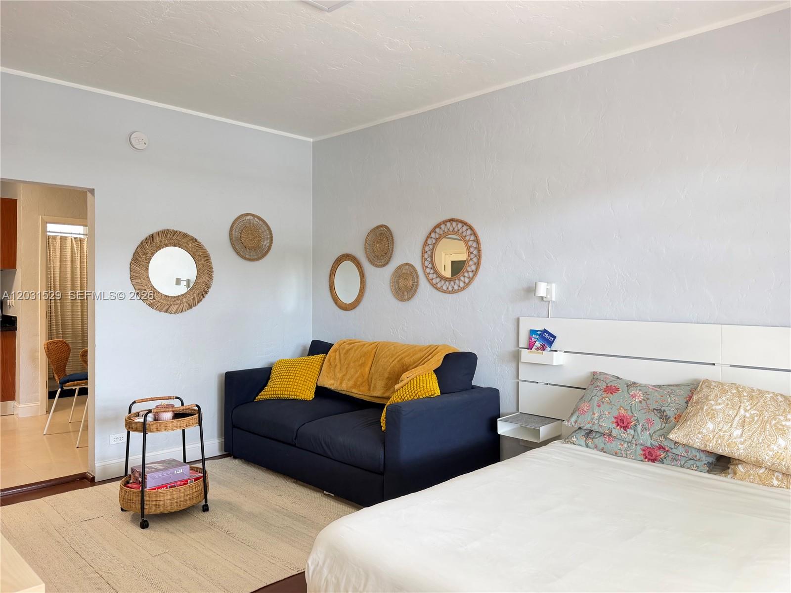 A bedroom features a dark blue sofa, a bed, and wall-mounted wicker decor — 500 14th St # 104, Miami Beach FL 33139, MIAMI BEACH, FL