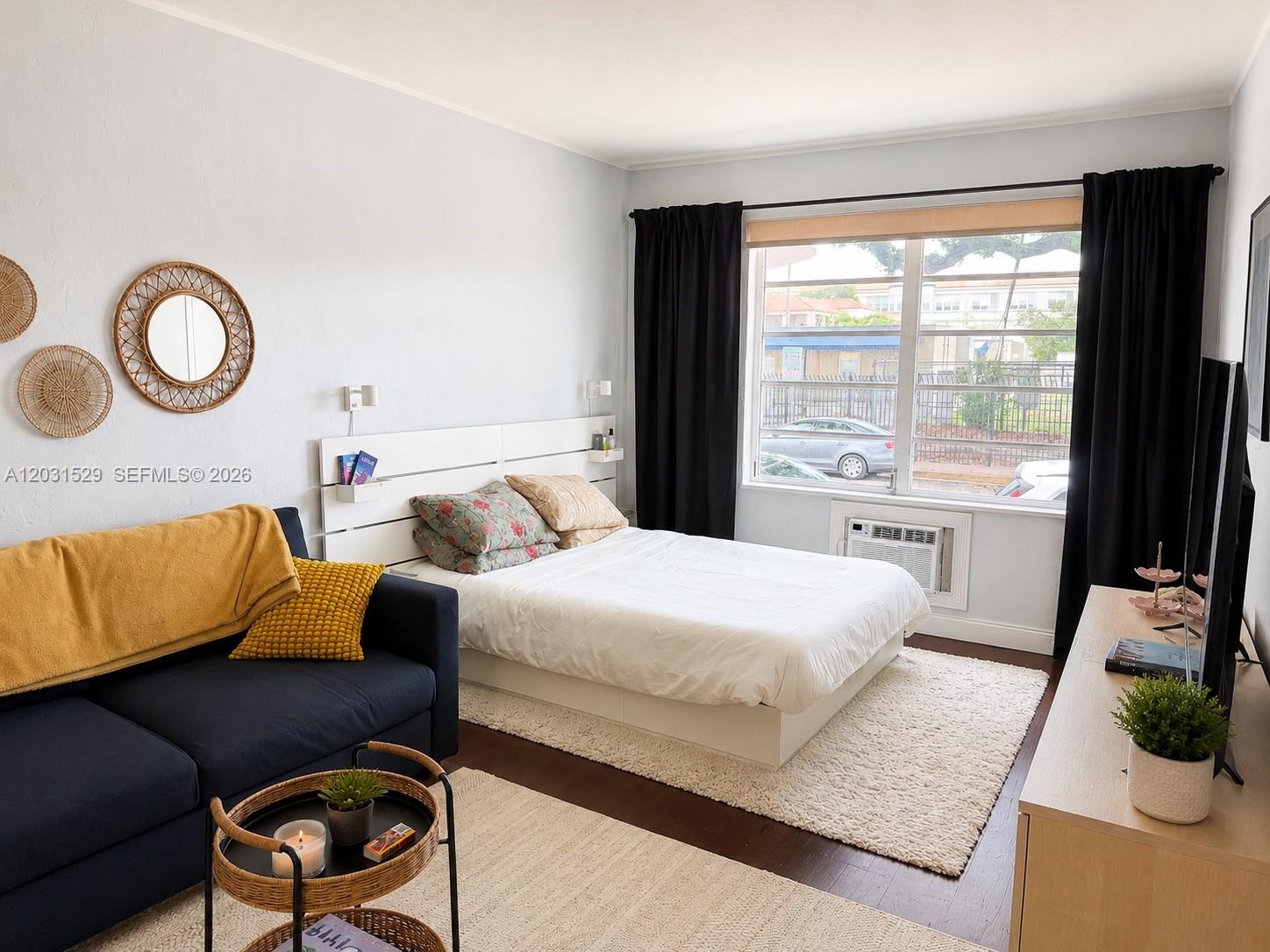 A studio apartment features a bed, a navy sofa, and a window with black curtains — 500 14th St # 104, Miami Beach FL 33139, MIAMI BEACH, FL