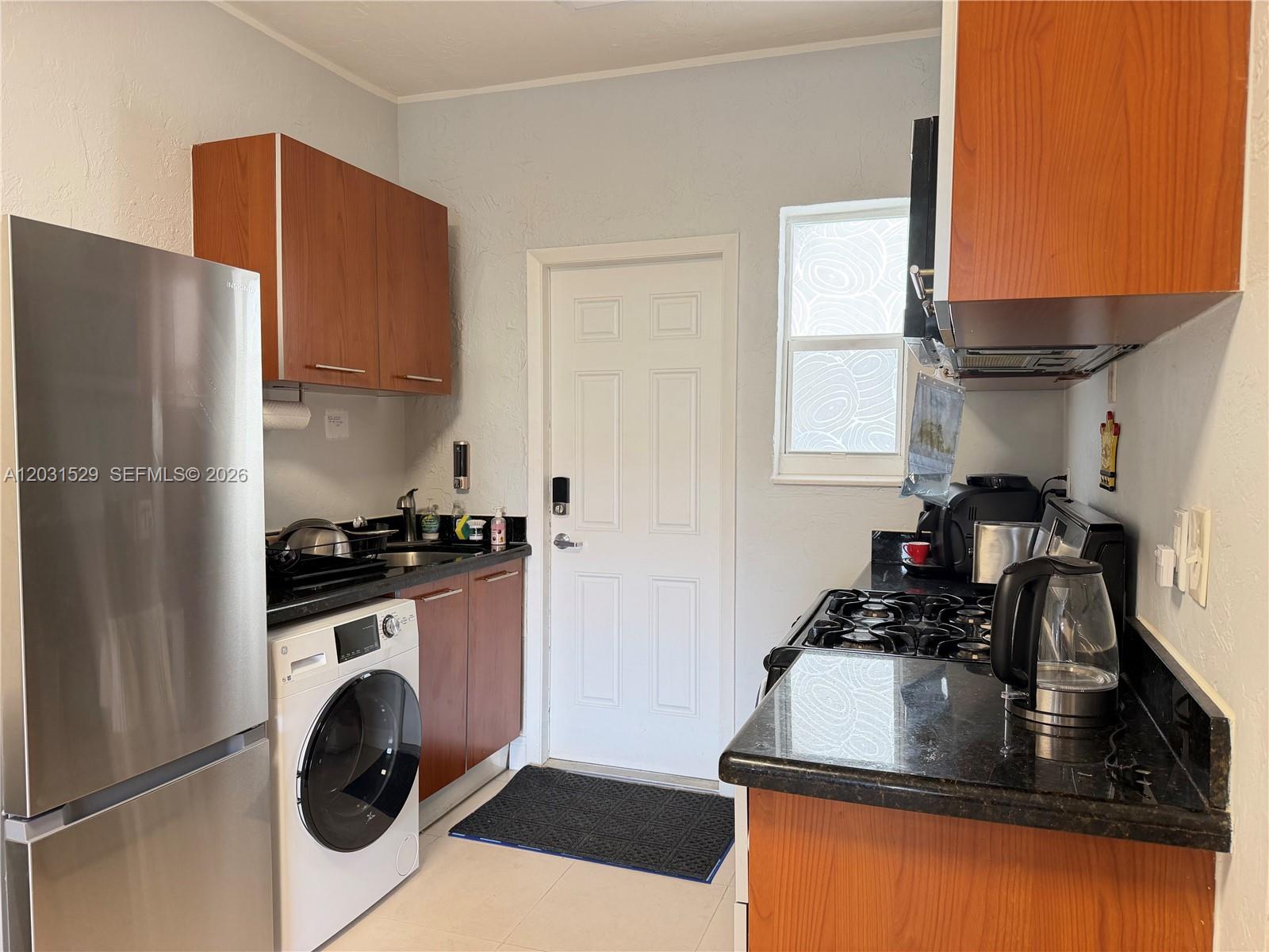 A small kitchen features wood cabinets, black countertops, stainless steel appliances, and a washer — 500 14th St # 104, Miami Beach FL 33139, MIAMI BEACH, FL