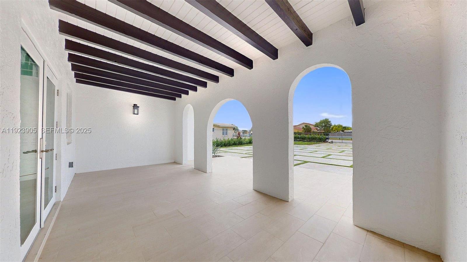A covered patio features white arched openings, dark wood ceiling beams, and tiled flooring — 3801 SW 132nd Ave, Miami FL 33175, MIAMI, FL
