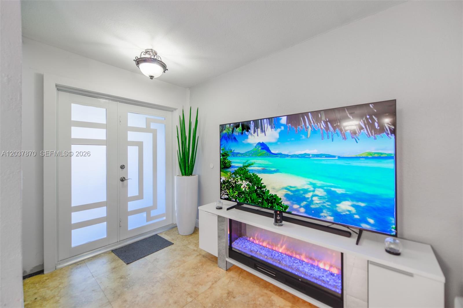 A room features a large television above an electric fireplace console and a glass door — 15216 SW 112th Pl, Miami FL 33157, MIAMI, FL