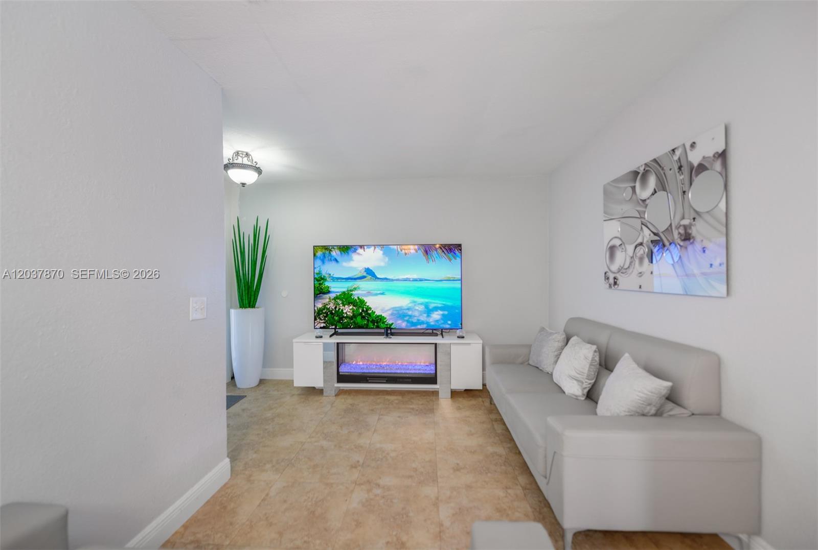 A living room features a grey sofa, a television on a fireplace console, and tile flooring — 15216 SW 112th Pl, Miami FL 33157, MIAMI, FL