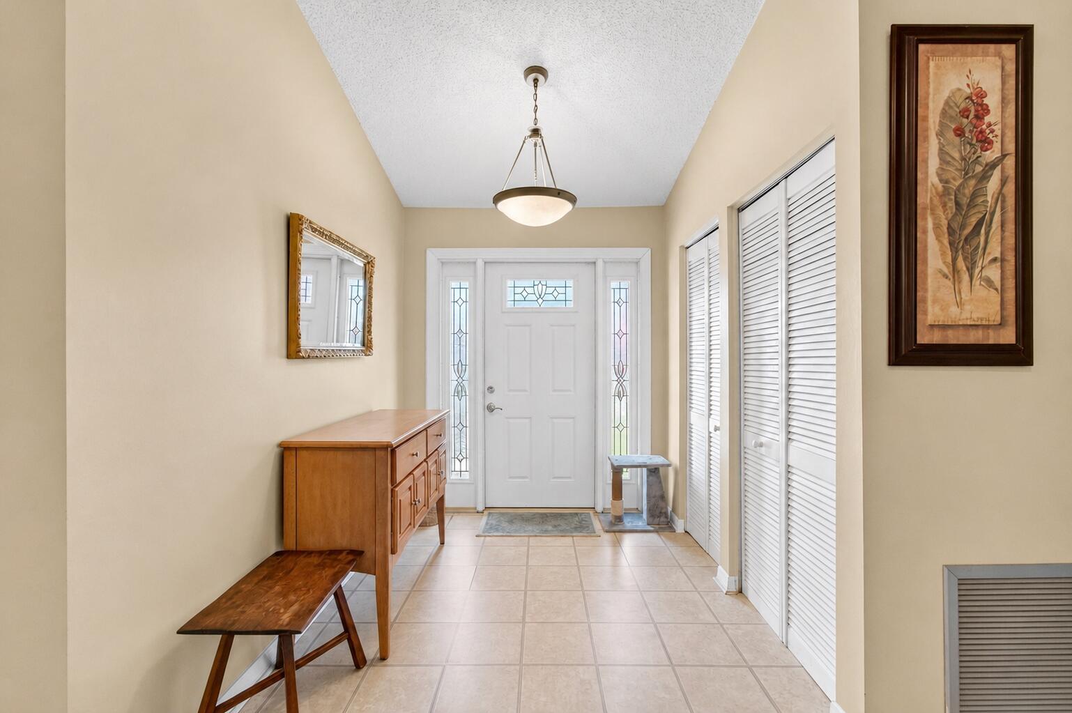A bright entryway features a white front door, tile flooring, a wooden console, and closets — 2400 SW 19th Avenue, Boynton Beach FL 33426, BOYNTON BEACH, FL
