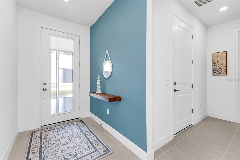 An entryway features a blue accent wall, a floating wooden shelf, and a patterned rug — 4400 LAKESIDE GROVE PLACE, NORTH PORT, FL