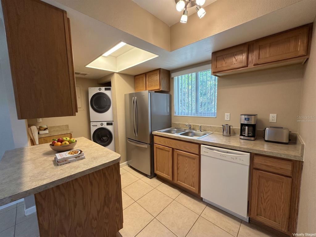 A kitchen with wood cabinets, stainless steel appliances, a stacked washer-dryer, and tile flooring — 5568 GREEN SHADOWS PLACE UNIT 21-1, ORLANDO, FL