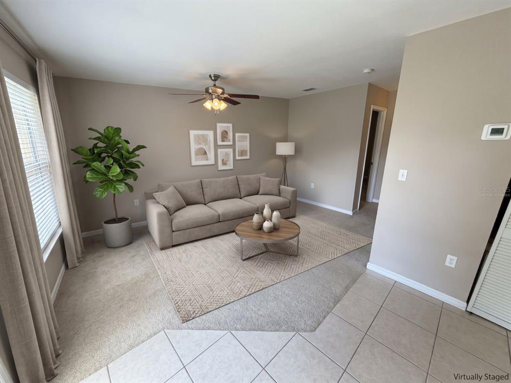 This virtually staged living room features a beige sofa, a round coffee table, and carpeting — 5568 GREEN SHADOWS PLACE UNIT 21-1, ORLANDO, FL