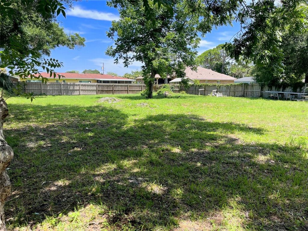 A grassy backyard features a large tree, a wooden fence, and neighboring houses — 707 CHERRY STREET, NEW SMYRNA BEACH, FL