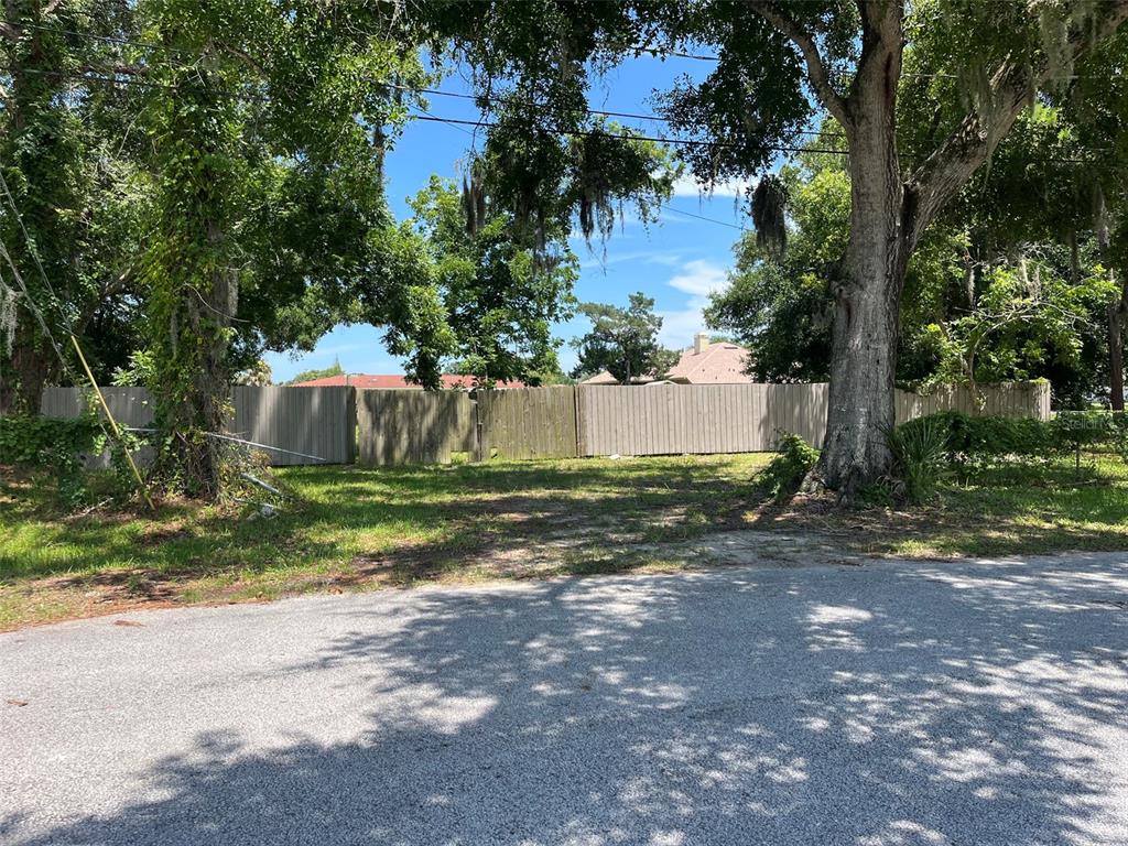 A vacant, grassy lot is enclosed by a wooden fence and surrounded by large trees — 707 CHERRY STREET, NEW SMYRNA BEACH, FL