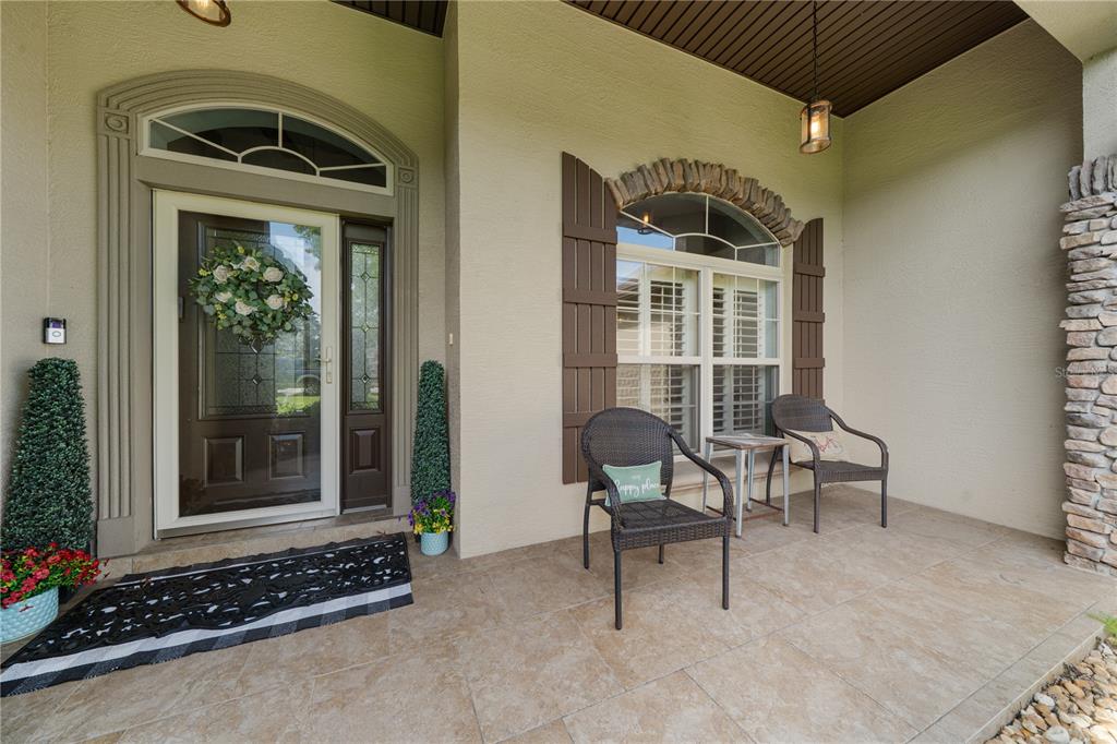 A covered front porch features tiled flooring, two wicker chairs, and a decorative front door — 4950 SW 114TH STREET ROAD, OCALA, FL