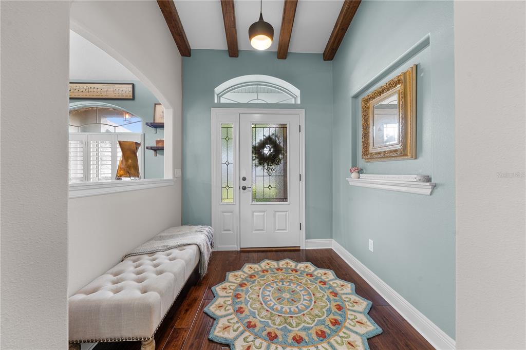 An entryway features a tufted bench, a round patterned rug, and wood-beamed ceilings — 4950 SW 114TH STREET ROAD, OCALA, FL