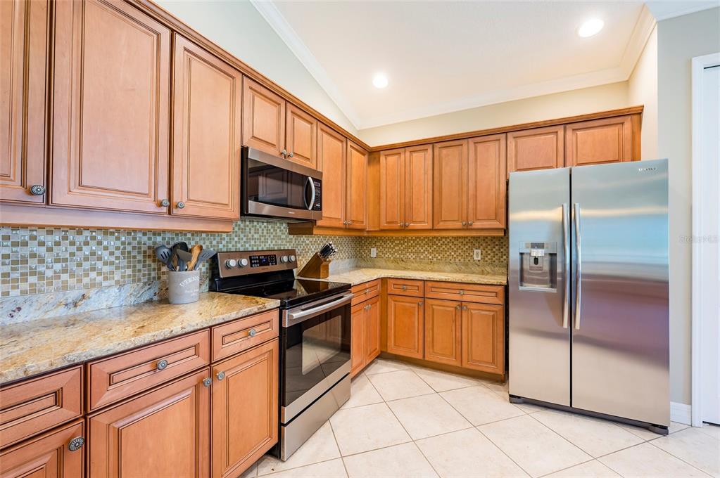A kitchen with wood cabinets, stainless steel appliances, granite countertops, and a tiled backsplash — 9453 NE DISCOVERY TERRACE UNIT 201C, BRADENTON, FL