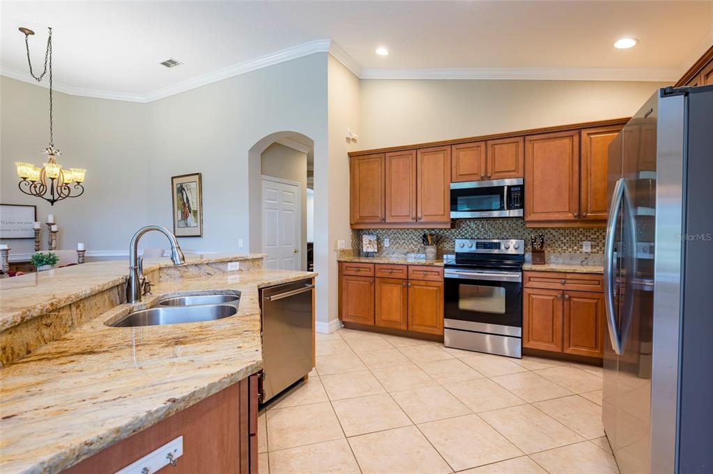 A kitchen features granite countertops, wood cabinetry, stainless steel appliances, and tile flooring — 9453 NE DISCOVERY TERRACE UNIT 201C, BRADENTON, FL
