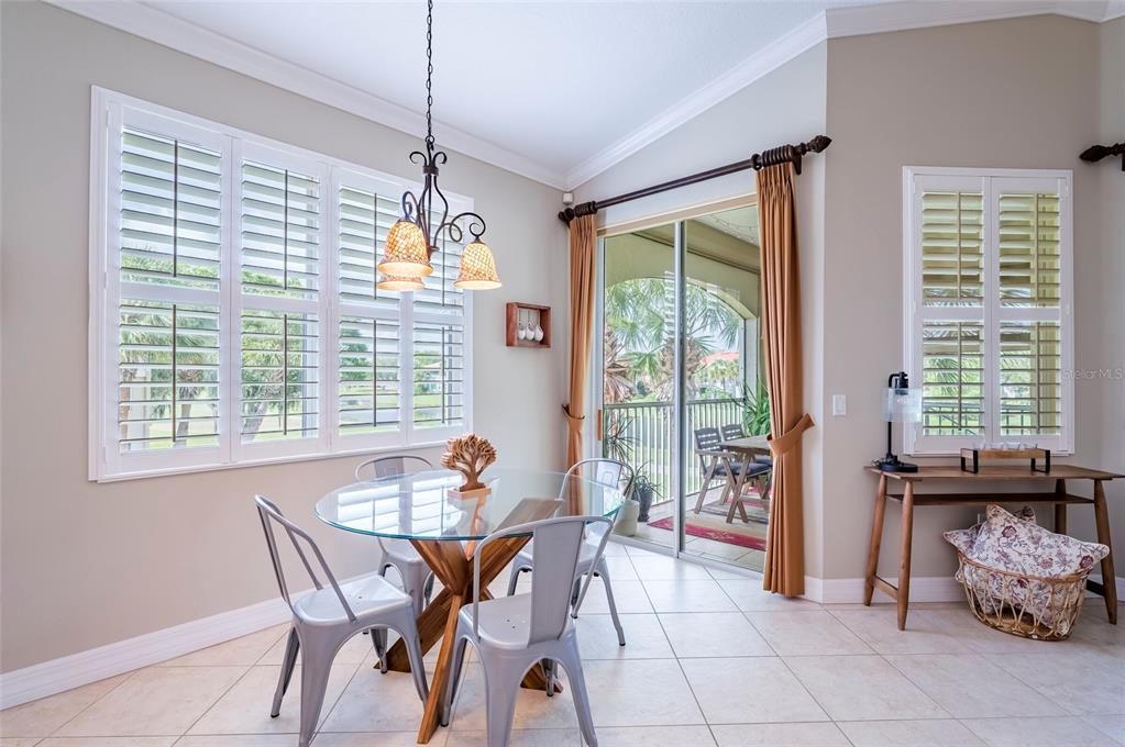 A dining area features a glass table, metal chairs, plantation shutters, and a sliding door — 9453 NE DISCOVERY TERRACE UNIT 201C, BRADENTON, FL