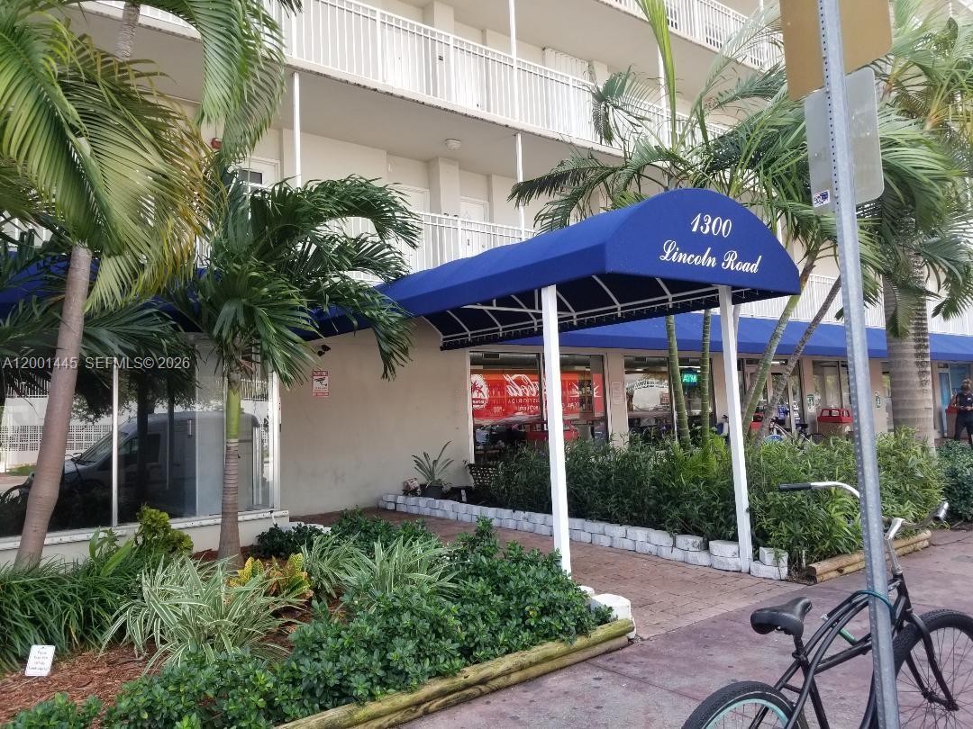 A blue awning with the address marks the entrance to a building with palm trees — 1300 Lincoln Rd # A301, Miami Beach FL 33139, MIAMI BEACH, FL