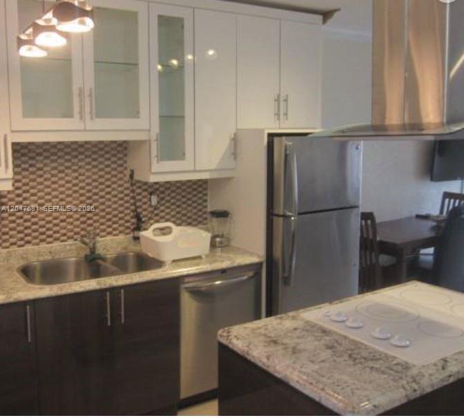 A kitchen features white upper cabinets, dark lower cabinets, granite countertops, and stainless steel appliances — 600 Layne Blvd # 115, Hallandale Beach FL 33009, HALLANDALE BEACH, FL