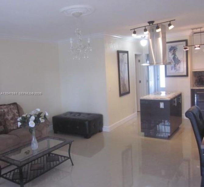 A living room with a glass coffee table, chandelier, and a kitchen island with hood — 600 Layne Blvd # 115, Hallandale Beach FL 33009, HALLANDALE BEACH, FL