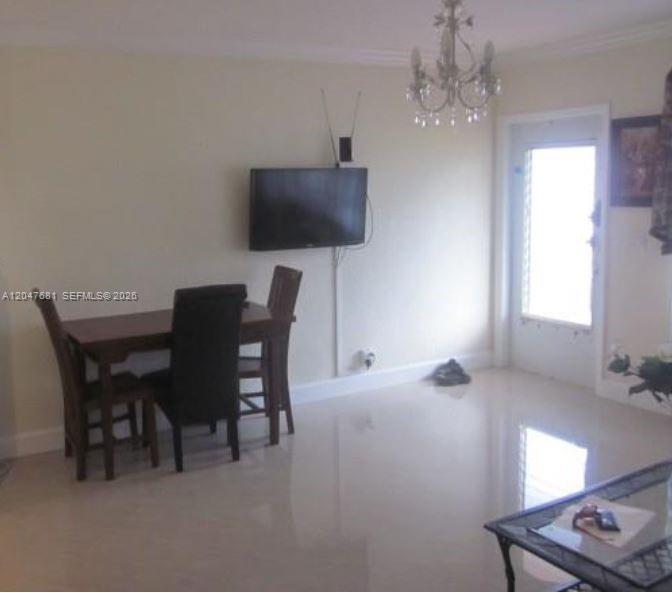A dining area features a wooden table, three chairs, a wall-mounted television, and tile flooring — 600 Layne Blvd # 115, Hallandale Beach FL 33009, HALLANDALE BEACH, FL