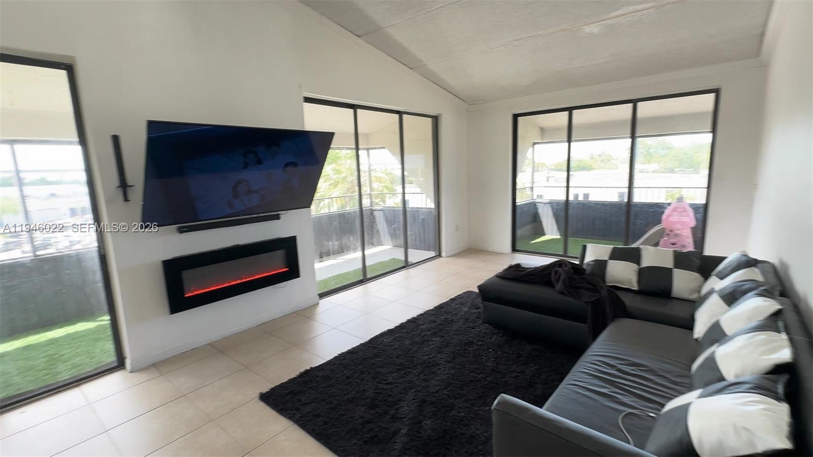 A living room features a wall-mounted television, an electric fireplace, tile floors, and sliding doors — 16220 NW 2nd Ave # 513, Miami FL 33169, MIAMI, FL
