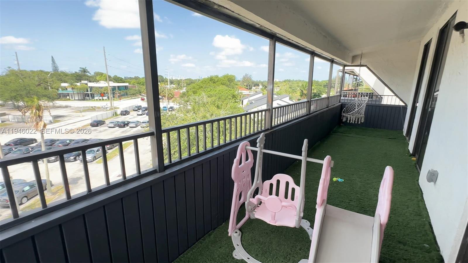 A balcony with artificial turf flooring features a children's swing set and a hanging chair — 16220 NW 2nd Ave # 513, Miami FL 33169, MIAMI, FL