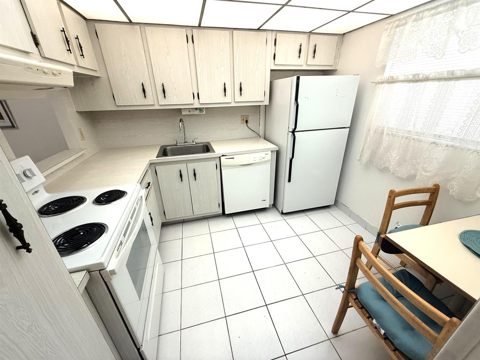 A kitchen with white appliances, light wood cabinets, white tile flooring, and a small dining table — 3050 Holiday Springs Boulevard # 111, Margate FL 33063, MARGATE, FL