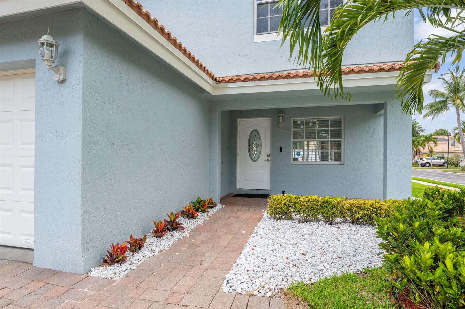 The exterior of a light blue house features a brick walkway, white gravel, and landscaping — 3460 Commodore Court, West Palm Beach FL 33411, WEST PALM BEACH, FL
