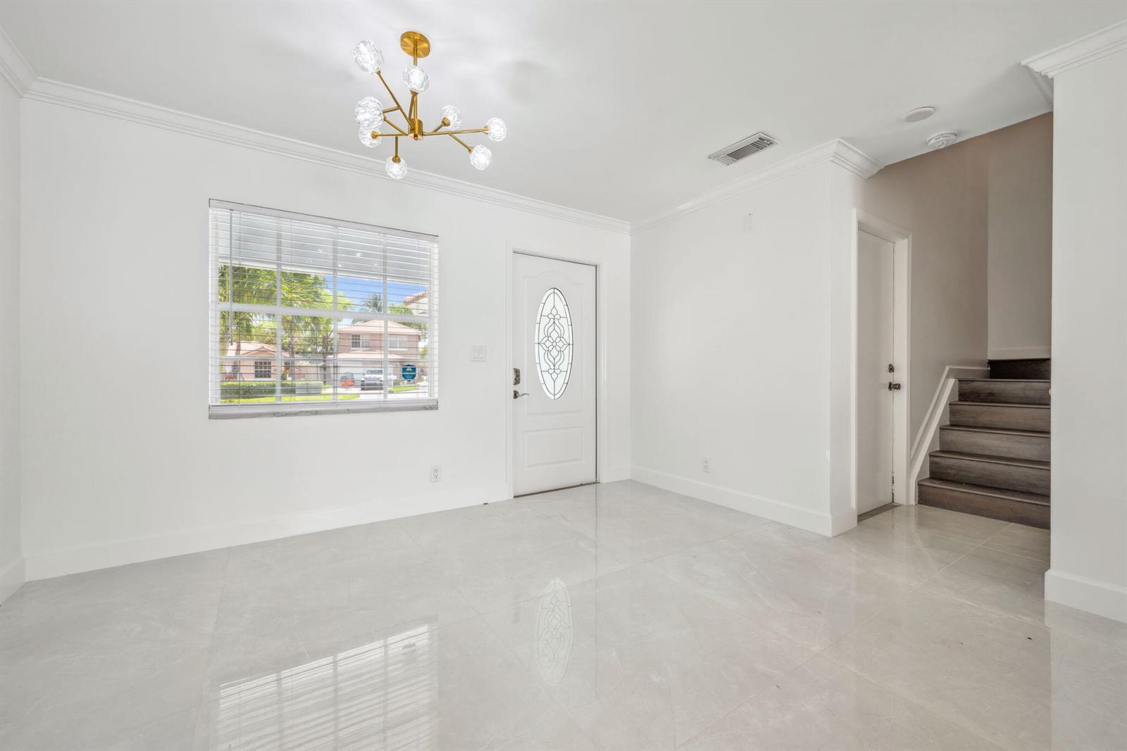 An entryway features white walls, light tile flooring, a modern chandelier, and a staircase — 3460 Commodore Court, West Palm Beach FL 33411, WEST PALM BEACH, FL
