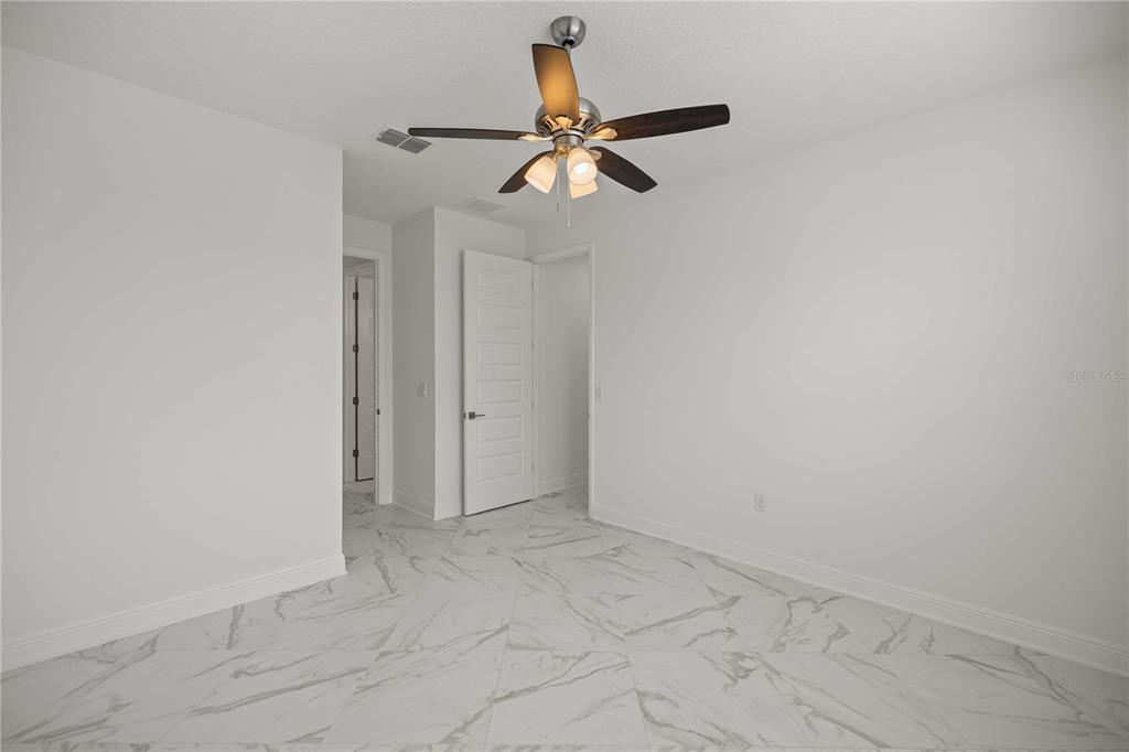 An empty room features white walls, a ceiling fan, and light-colored marble-patterned tile flooring — 8418 SW 93RD CIRCLE, OCALA, FL