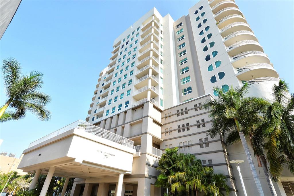 A low-angle exterior view of a tall, modern residential building with balconies and palm trees — 1771 RINGLING BOULEVARD UNIT 603, SARASOTA, FL