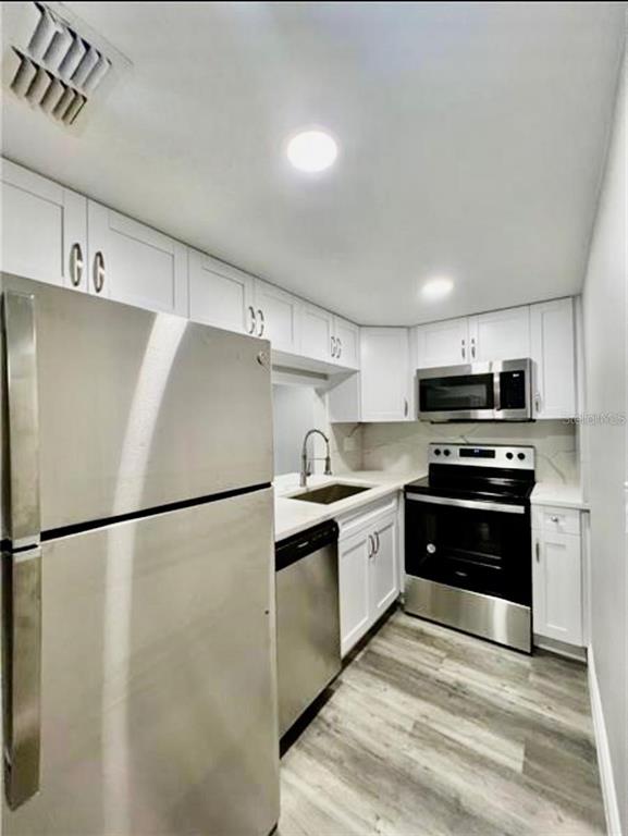 A kitchen with white cabinets, stainless steel appliances, and wood-look flooring — 7108 WATERSIDE DRIVE, TAMPA, FL