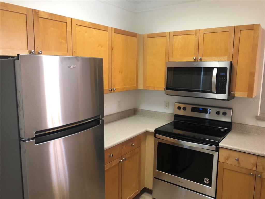 A kitchen features light wood cabinets, stainless steel appliances, and light-colored countertops — 8848 VILLA VIEW CIRCLE UNIT 203, ORLANDO, FL
