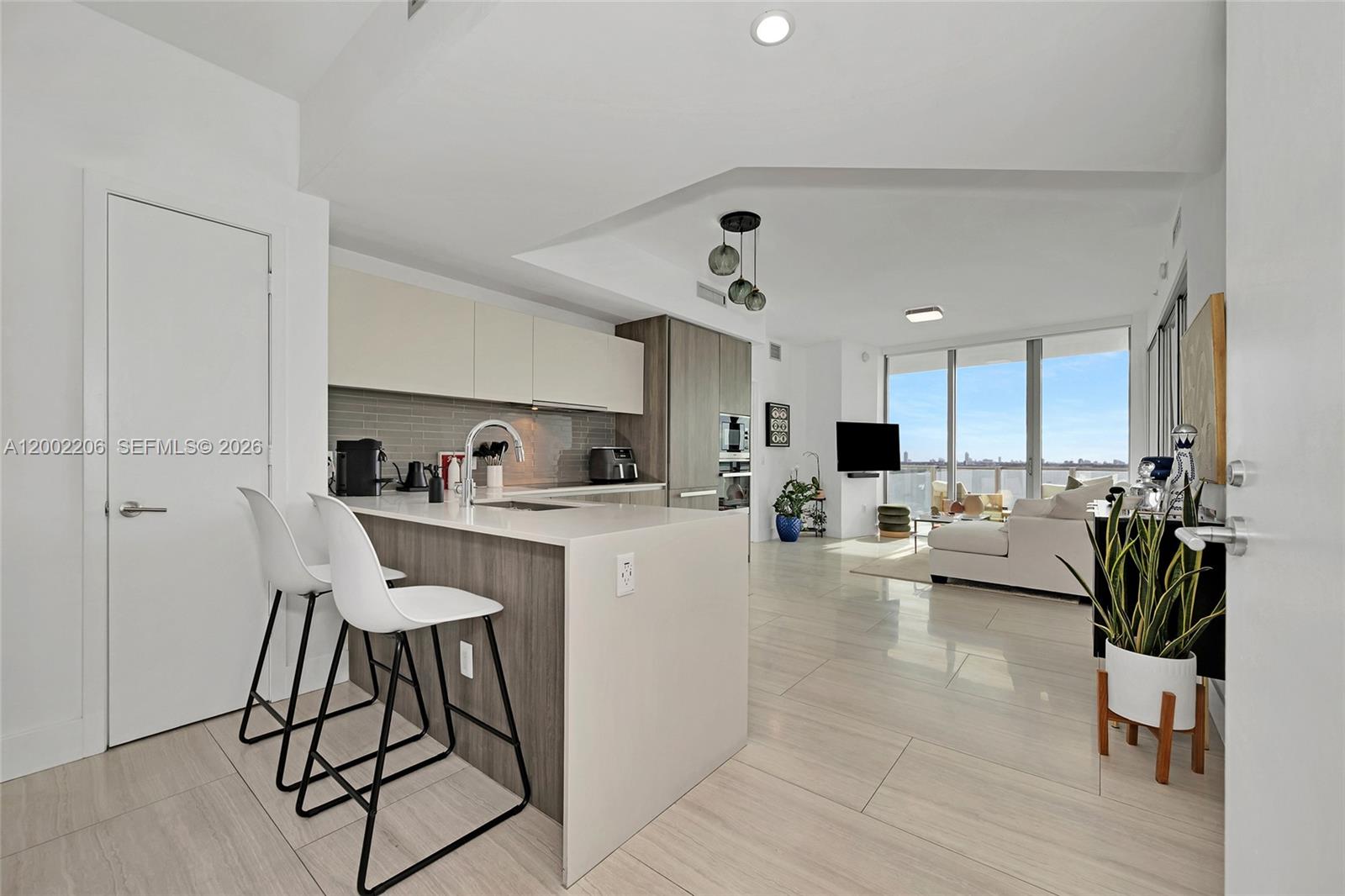 A modern kitchen with a breakfast bar overlooks a living area with floor-to-ceiling windows — 2900 NE 7th Ave # 1505, Miami FL 33137, MIAMI, FL