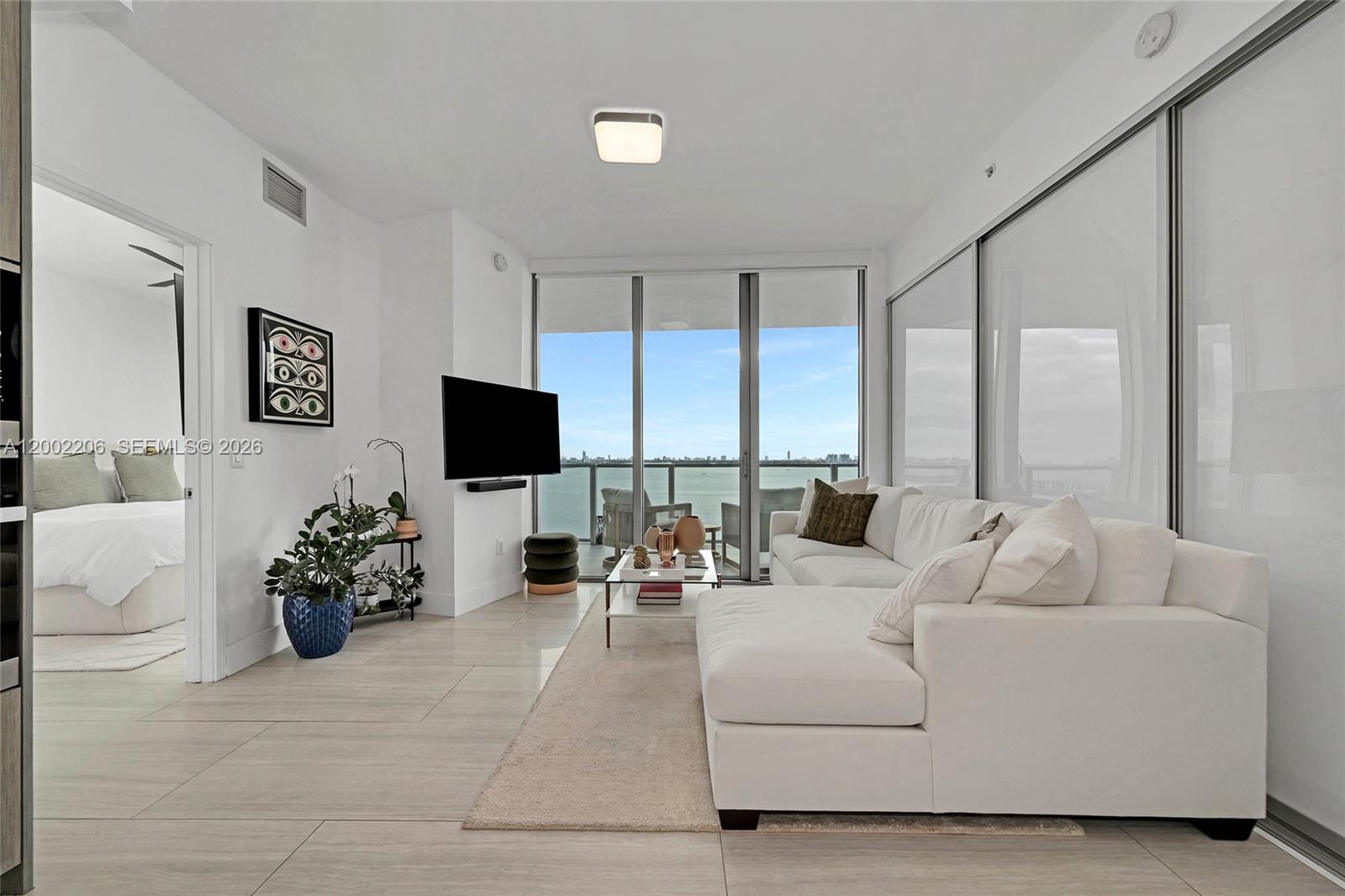 A modern living room features a white sectional sofa, tile flooring, and floor-to-ceiling balcony windows — 2900 NE 7th Ave # 1505, Miami FL 33137, MIAMI, FL